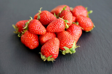 Fresh red strawberries with leaves on slate board. Pile of ripe strawberry for background