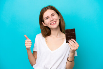 Young English woman isolated on blue background taking a chocolate tablet and with thumb up