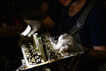 Partial view of mechanic in gloves holding lamp while inspecting damaged car engine 