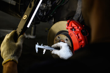 Partial view of auto mechanic holding caliper and lamp near disc brake in garage 
