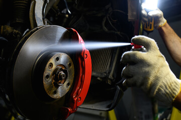 Partial shot of auto mechanic spraying disc brake liquid on wheel and holding lamp in garage 