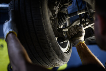 Fototapeta na wymiar Blurred repairman in gloves using wrench while working with car wheel in garage 