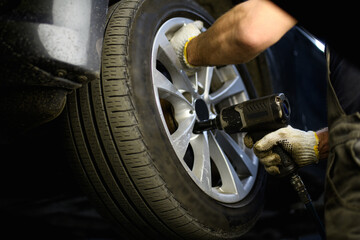 Repairman using pneumatic wrench while changing car wheel in garage 