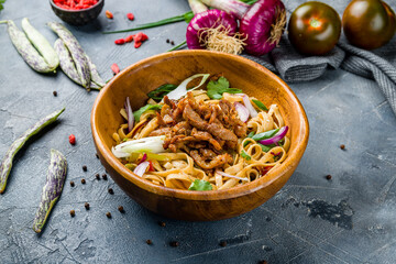 Udon noodles with pork and vegetables on wooden bowl on grey table