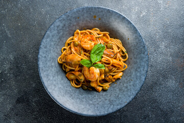 Pasta spaghetti with seafood, squid, shrimps and mussels on tomato sauce on grey plate on dark grey table top view