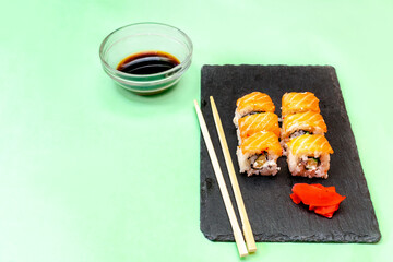 Fish sushi rolls with salmon, wasabi and chopsticks on black cutting serving board on green background with copy space. Seafood, Food service from restaurant concept, flatlay