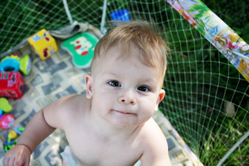 Cute little baby who can't walk yet is in play pen. Naked baby stands in an play pen and looks up....