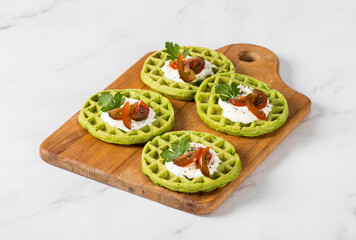 Spinach waffles with cottage cheese, cherry tomatoes and parsley, on a wooden board. Light background
