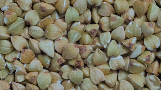 Close up: heap of uncooked green buckwheat groats on slow rotating surface - top view, macro. Healthy food, organic and gluten free concept