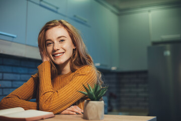 Fototapeta na wymiar Caucasian redheaded woman with happy facial expression looking at camera with joy while reading a book. Front view portrait. Beautiful young girl. Beauty face
