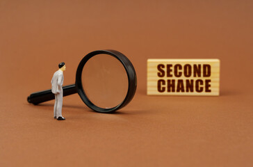 A figurine of a businesswoman looks through a magnifying glass at a block with the inscription - SECOND CHANCE