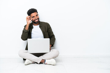 Young Brazilian man with a laptop sitting on the floor isolated on white with glasses and happy