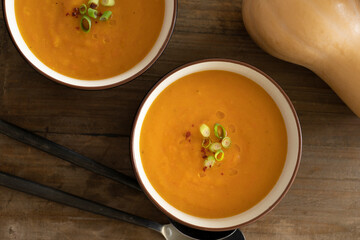 Top view of bowl with delicious pumpkin soup, ingredients like pumpkin and spoons on a wooden table
