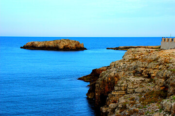 Fantastic scenery with a high massive coast of Polignano a Mare and a rocky island washed by the calm Adriatic sea reflecting the azure sky during the golden hour
