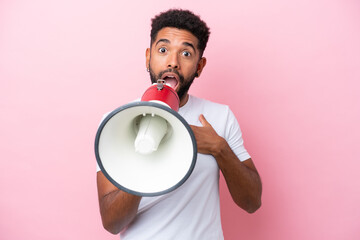 Young Brazilian man isolated on pink background shouting through a megaphone with surprised expression