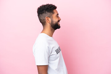 Young volunteer man isolated on pink background laughing in lateral position