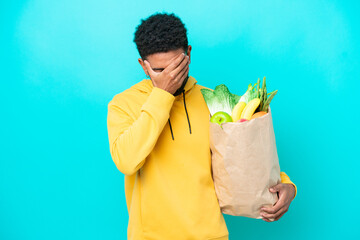 Young Brazilian man taking a bag of takeaway food isolated on blue background with tired and sick expression