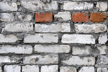 An old and damaged wall made of white and orange bricks as a background
