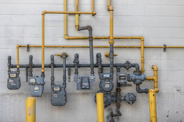 Natural gas distribution with meters, pipes and manifolds mounted on a cinder block exterior wall of a multi-unit commercial building, daytime, nobody - obrazy, fototapety, plakaty