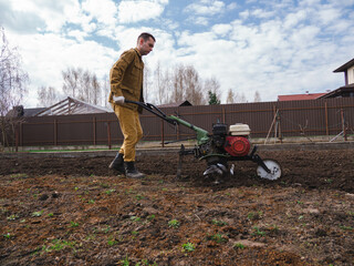 Farmer cultivates the ground soil in the garden using a motor cultivator or tiller tractor. Modern...