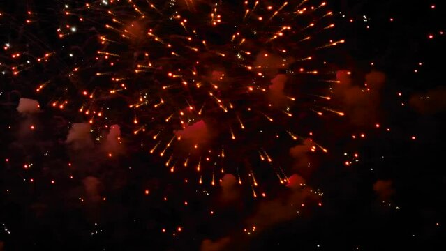 Colorful bright red and orange fireworks in dark sky at night. Evening time, low light. Holiday, celebration, entertainment, abstract and anniversary concept