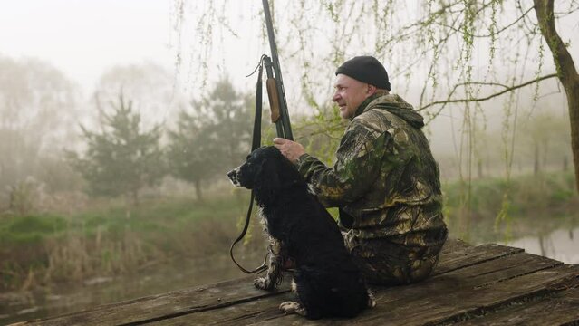 morning hunt on a background of misty lake. a hunter with a weapon and a hunting dog are sitting waiting for prey