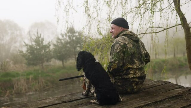 morning hunt on a background of misty lake. hunting dog with a hunter who puts his weapon on his knees sitting waiting for prey