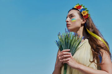 Beautiful Ukrainian woman in floral crown holding bunch of flowers with sky in the background