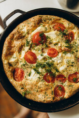 cooked frittata with tomatoes and pieces of meat in a frying pan top view. frittata ready to eat close-up. ready-made egg omelette with greens and cherry tomatoes in a pan.