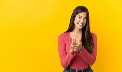 Teenager Brazilian girl over isolated yellow background applauding after presentation in a...