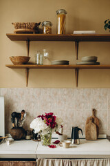 kitchen interior details. a bouquet of peonies in a transparent vase on a kitchen countertop. hanging wooden shelves with kitchen utensils