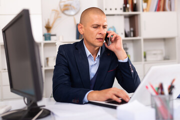 Positive man in formalwear talking on mobile phone at company office