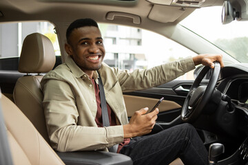 Handsome young man with smartphone near modern car outdoors