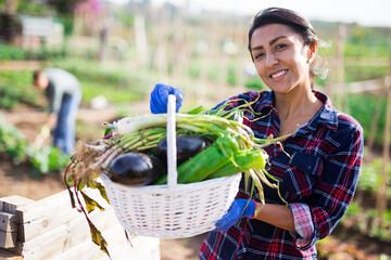 Smiling hispanic female gardener holding fresh greens and vegetables grown in her home garden
