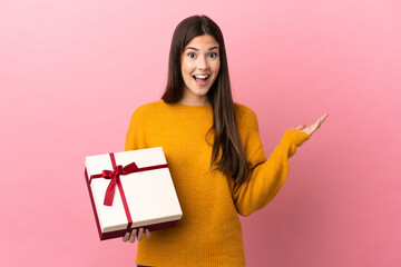 Teenager Brazilian girl holding a gift over isolated pink background with shocked facial expression