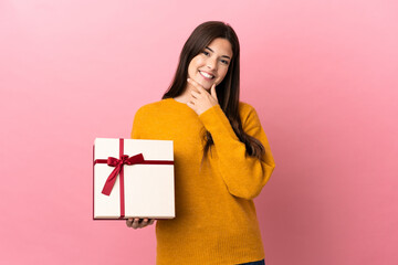 Teenager Brazilian girl holding a gift over isolated pink background happy and smiling