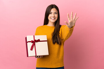 Teenager Brazilian girl holding a gift over isolated pink background counting five with fingers