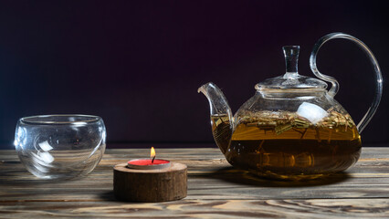 Hot herbal tea in glass teapot on wooden table on dark background. Traditional herbal drink. Place for text or design.