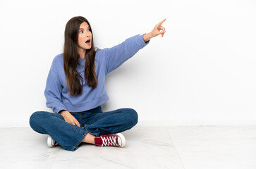 Young woman sitting on the floor pointing away