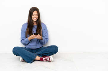 Young woman sitting on the floor sending a message with the mobile