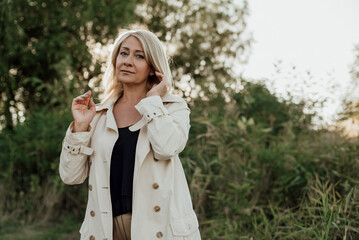 A beautiful adult woman with blond hair and a light raincoat smiles