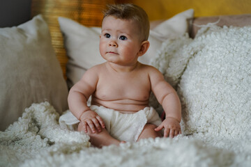 sweet adorable naked half year old baby boy sitting wrapped in white towel at home on the couch in...