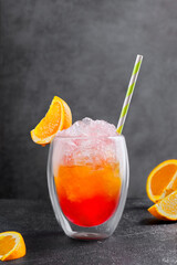 Tequila sunrise with crushed ice and fresh orange slice in glass standing on black table in bar. Alcohol drink made of citrus fruit with straw on grey background.