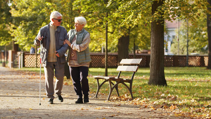  Woman leads her blind husband in park autumn full shot copy space . High quality photo