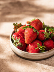 Delicious strawberries in a ceramic plate on brown textured background with beautiful shadows