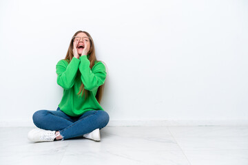 Young caucasian woman sitting on the floor isolated on white background shouting and announcing something