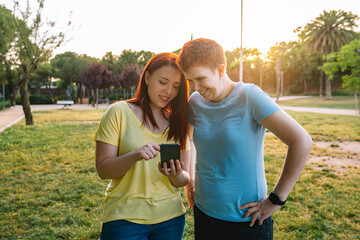 two great friends looking at their smartphones while sharing a relaxing moment in a public park at...