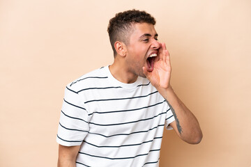 Young Brazilian man isolated on beige background shouting with mouth wide open to the side