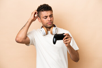 Fototapeta na wymiar Young Brazilian man playing with a video game controller isolated on beige background having doubts