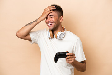 Fototapeta na wymiar Young Brazilian man playing with a video game controller isolated on beige background smiling a lot